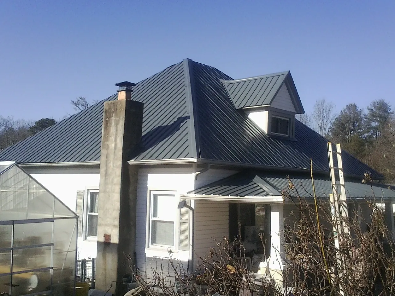 Dark blue standing seam metal roof on a white farmhouse with dormer — Slate & Tile Roof Repair by Roofing Brothers in North East