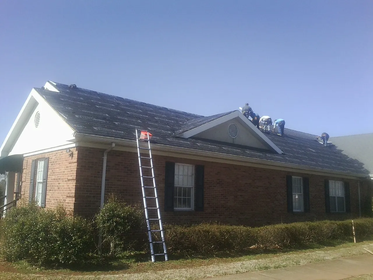 Crew tearing shingles off a brick ranch roof with a ladder set — Emergency Roof Repair work by our crew in North East