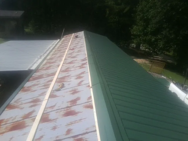 Old rusted panels beside newly installed green metal roofing — Wind Damage Roof Repair by Roofing Brothers in North East