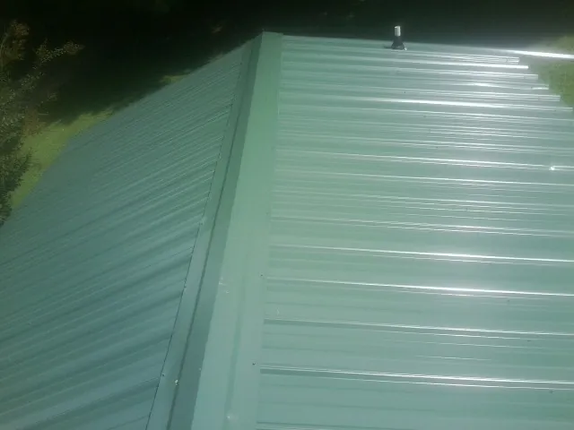 New green metal panels meeting at the ridge of a roof — Flat Roof Repair work by our crew in North East