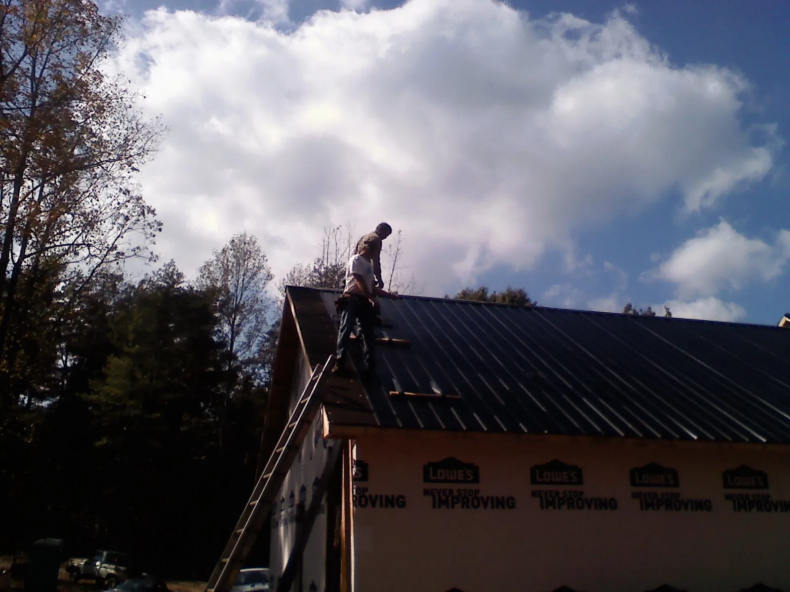 Roofer fastening dark metal panels high against a cloudy sky, from a Roof Inspection job in North East