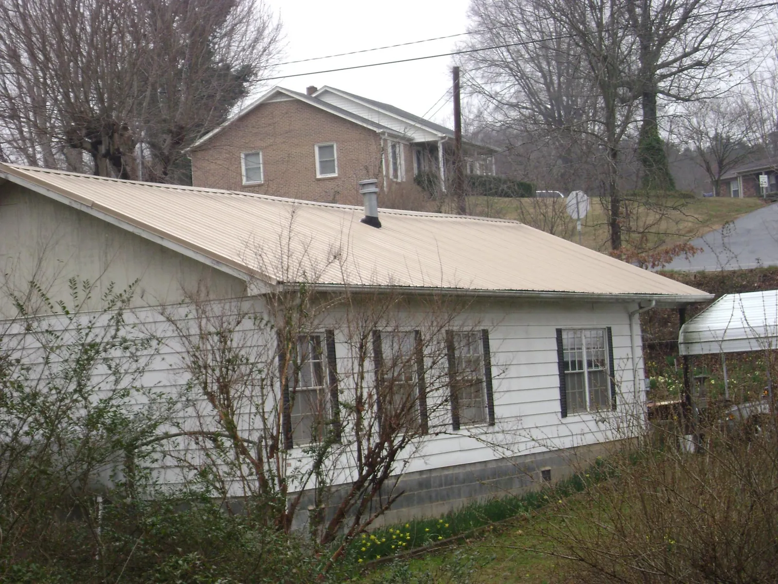 Tan metal roof on a white sided house set into a hillside — Commercial Roofing by Roofing Brothers in North East