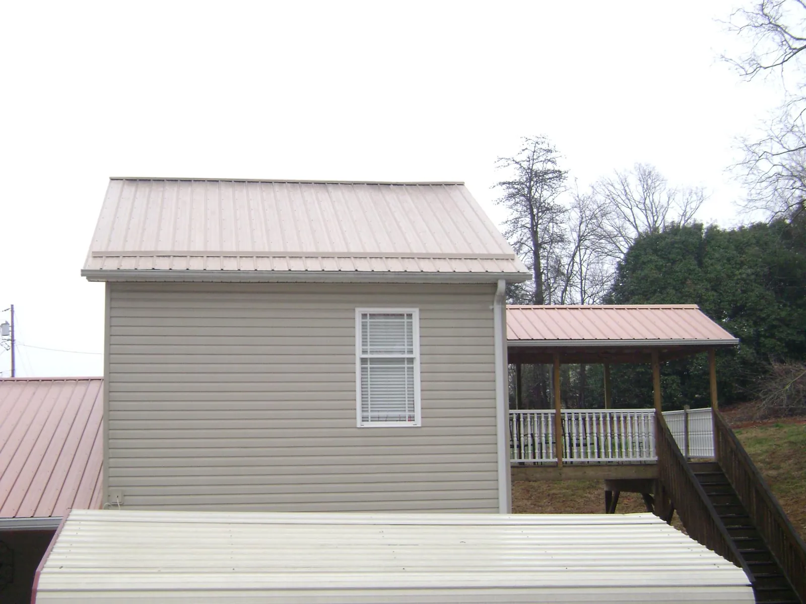 Tan metal roofs on a two story addition and attached porch, from a Roof Replacement job in North East